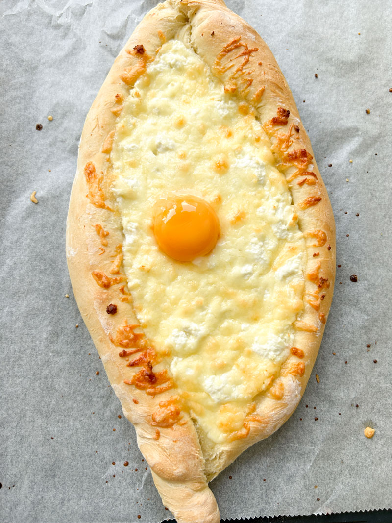 Khachapuri after baking, with melted cheeses, golden brown edges and a runny egg yolk.