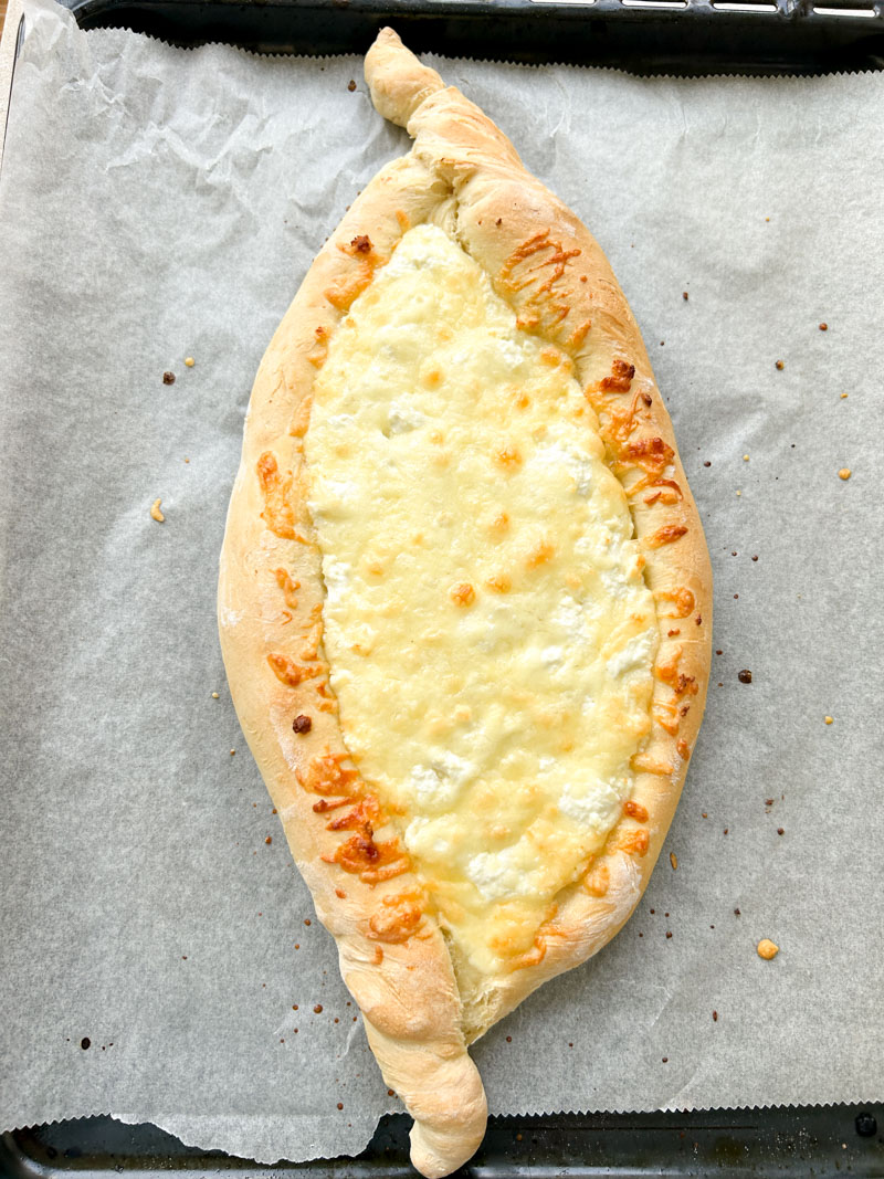 Khachapuri after baking, with melted cheeses and golden brown edges.