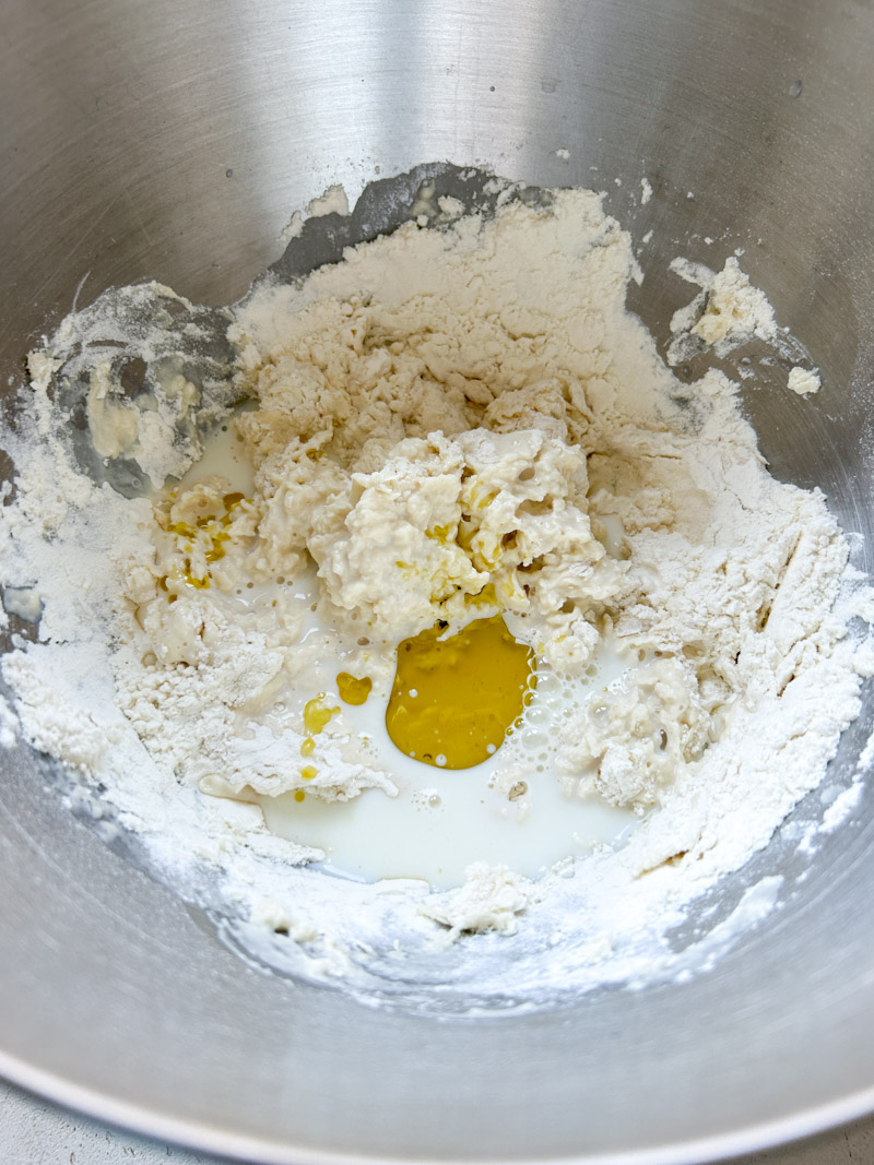 Olive oil added to the flour and water mixture, in the stand mixer's bowl.