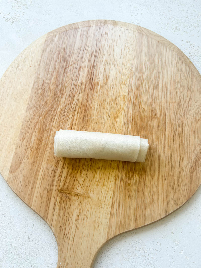 Pliage du samoussa en forme de cigare terminé. Il est posé sur la planche en bois ronde.
