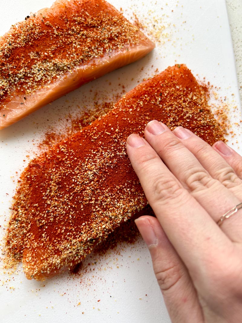One hand massaging the seasoning on a salmon fillet.
