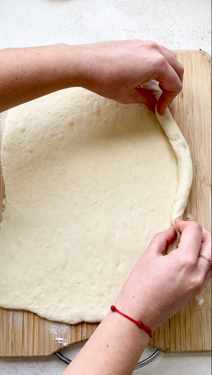 Two hands roll the edges into the typical Khachapuri boat shape.