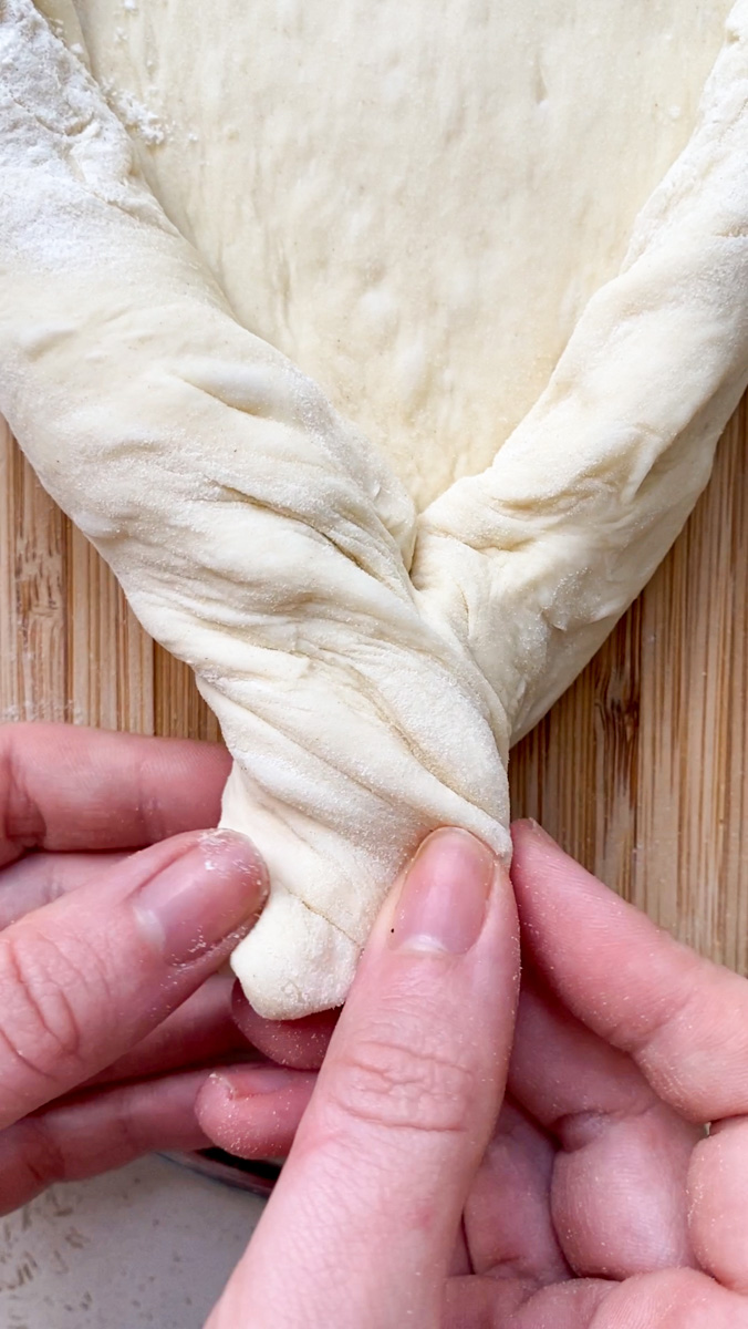 Two hands twist the edges of the Khachapuri.
