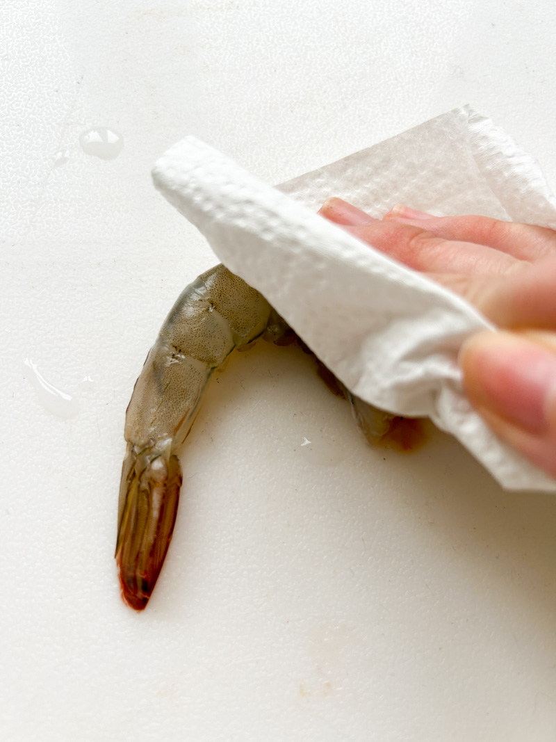 Paper towels dabbed on a shrimp, on a white cutting board.