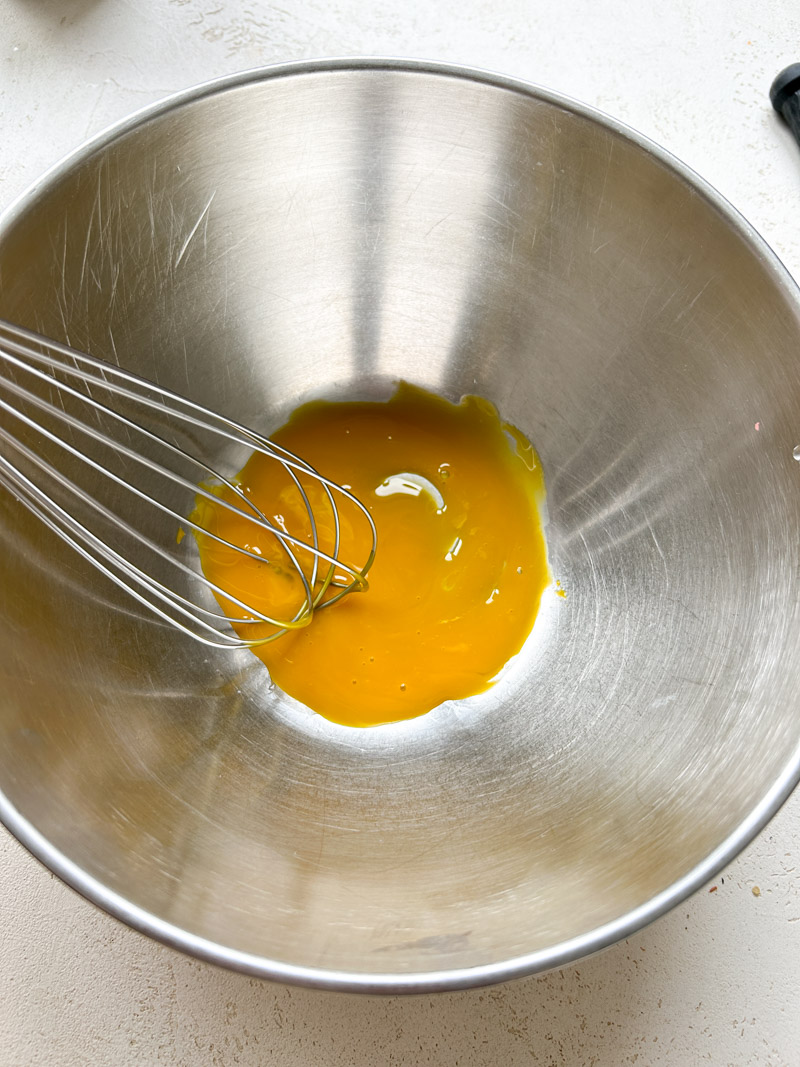 A whisk beating the egg yolk in a large bowl.