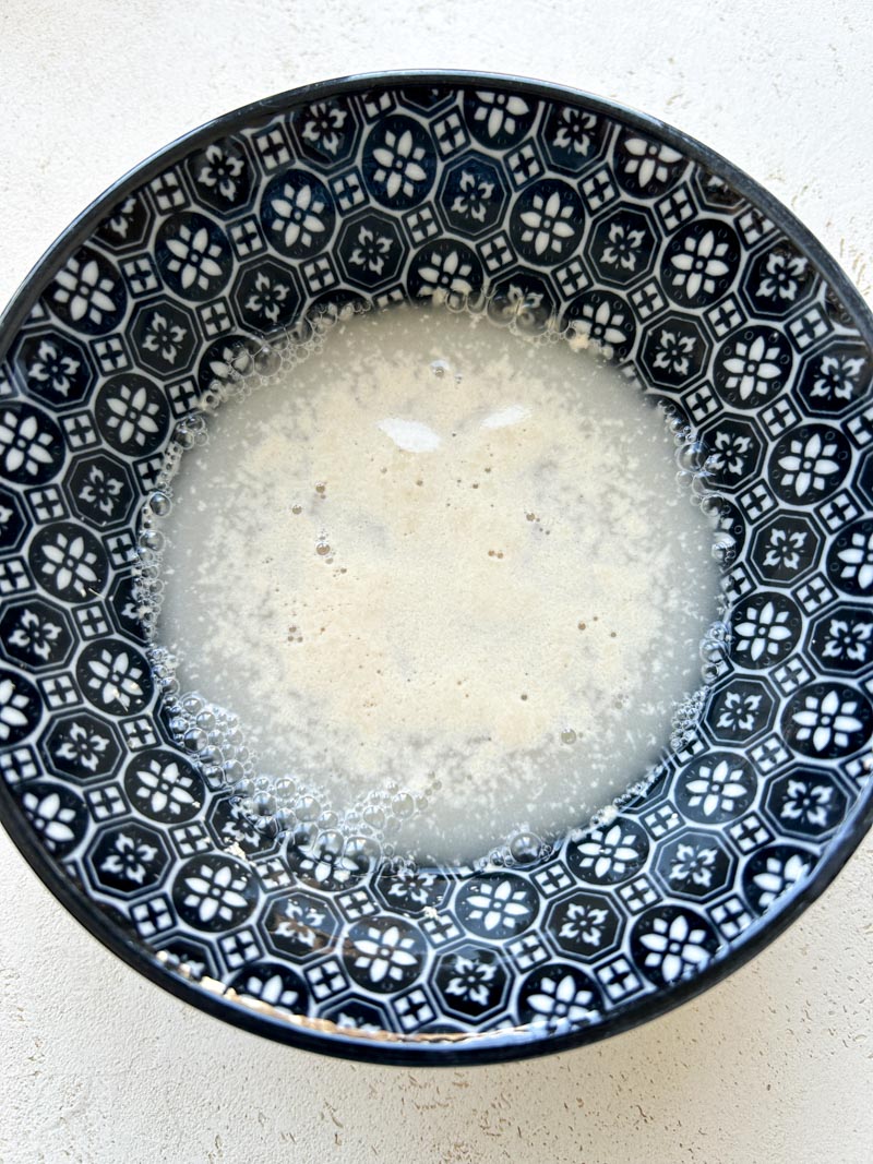 L'eau, le sucre et la levure boulangère sont mélangés dans un bol bleu, après un repos de 10 minutes.