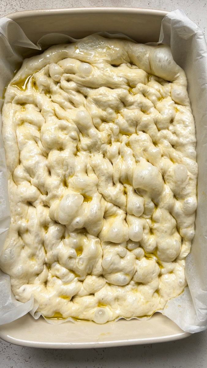 Dough in the baking dish, with holes and large air bubbles.