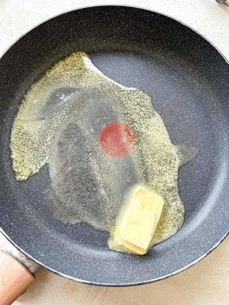 Beurre qui fond dans une grande poêle grise.