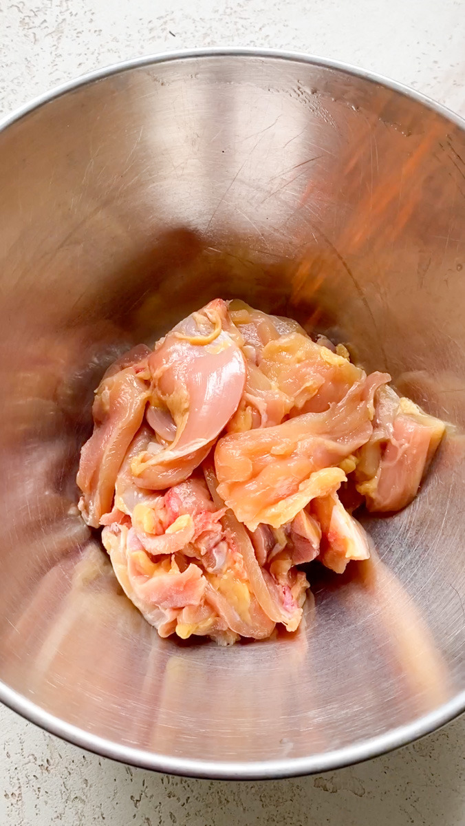 Hauts de cuisse de poulet coupés en morceaux et mis dans un bol en inox.