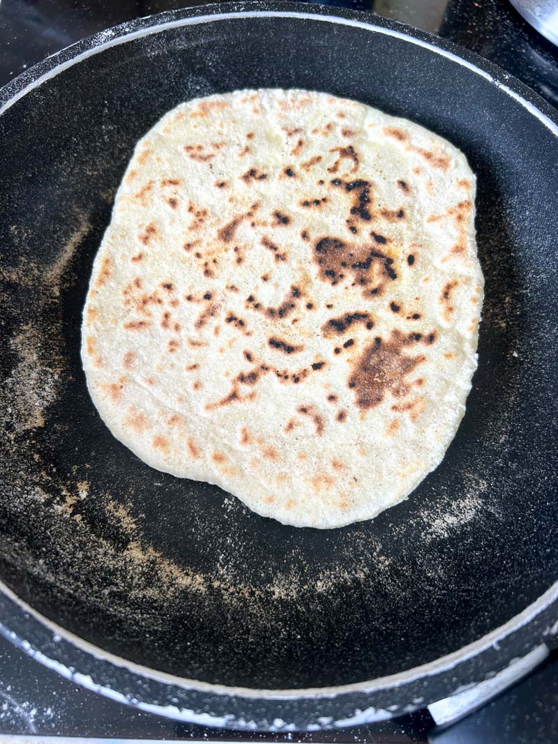 Cheese naan cooked on the second side, in a black pan.
