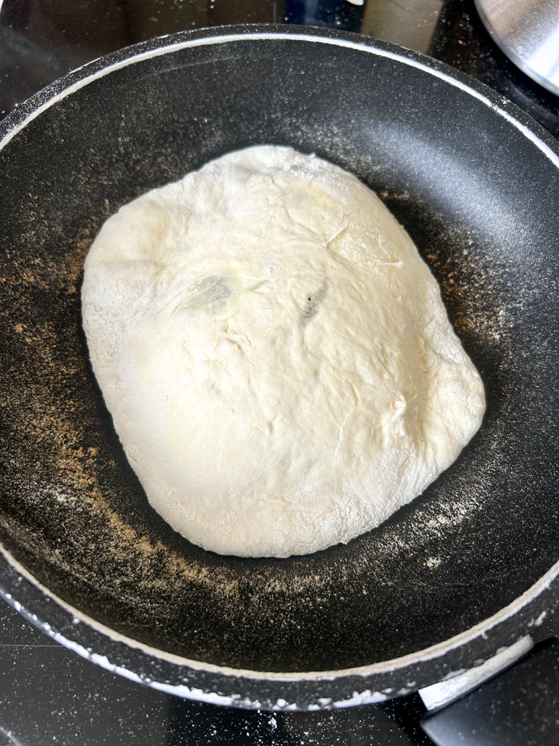 Cheese naan cooking in a black pan.