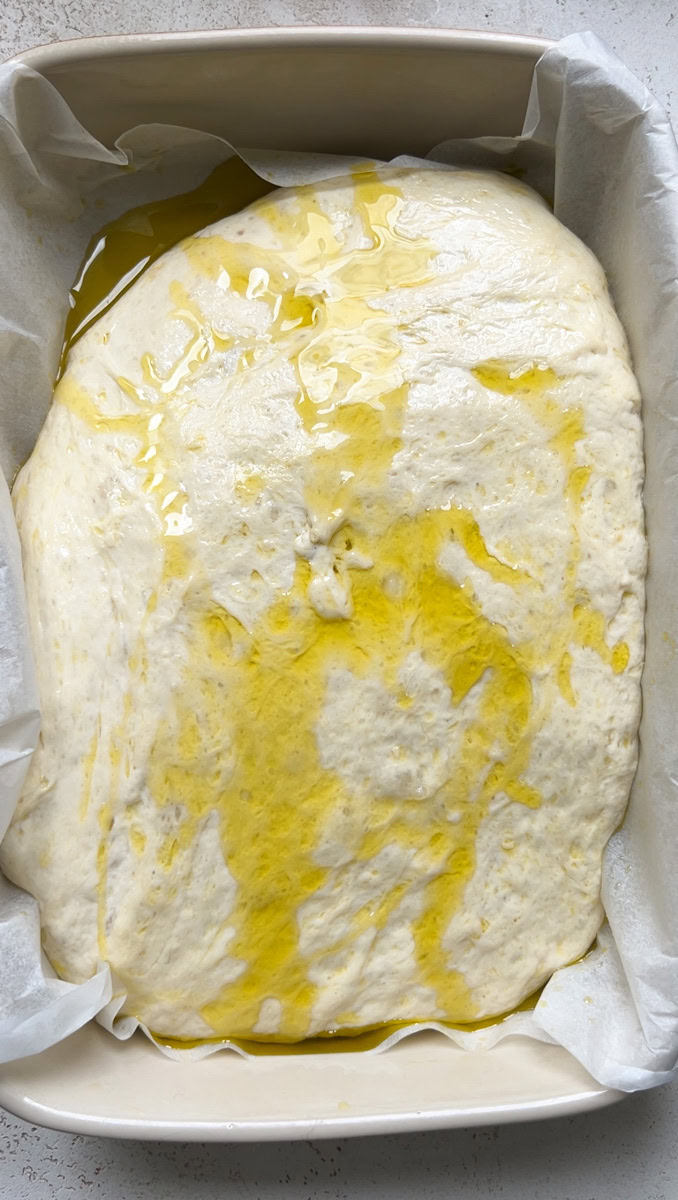 La pâte qui prend toute la place dans le plat, après sa deuxième levée, recouverte d'huile d'olive.