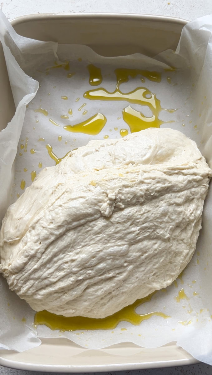 Dough in a baking dish with parchment paper and olive oil.