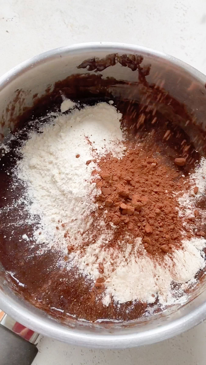 Flour and cocoa powder added to the saucepan of melted chocolate, butter, sugar and beaten eggs.