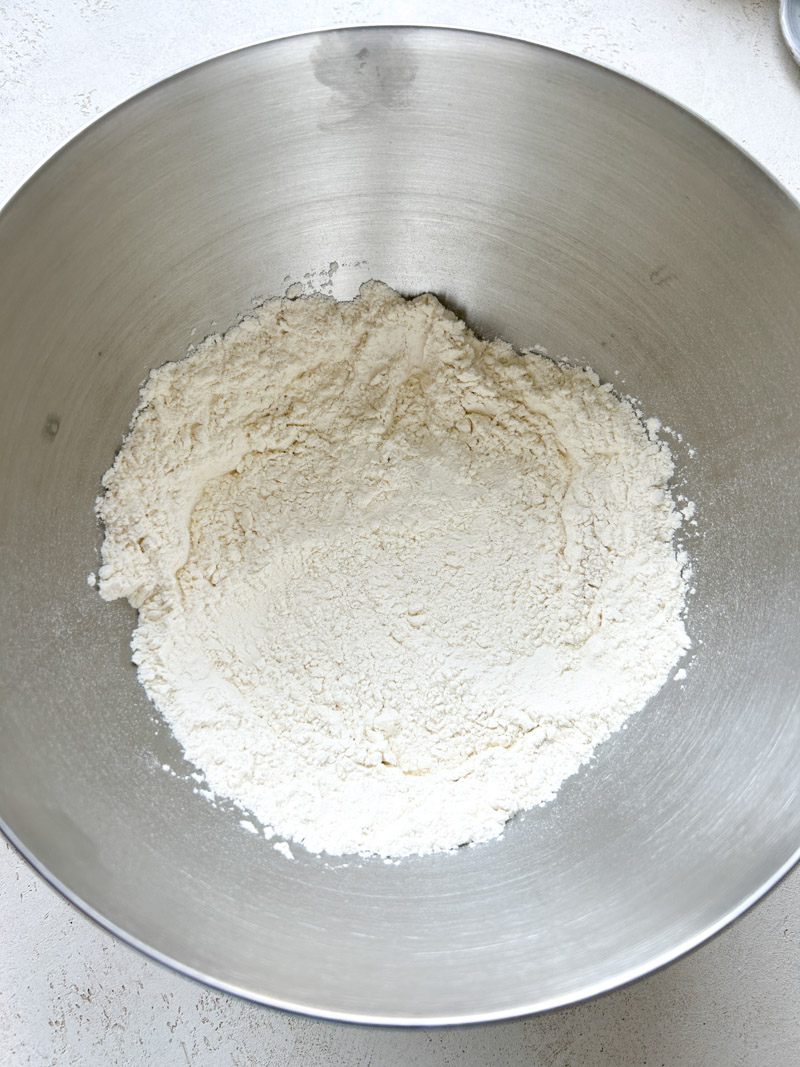 Flour and instant dry yeast mixed in a large stainless steel bowl.