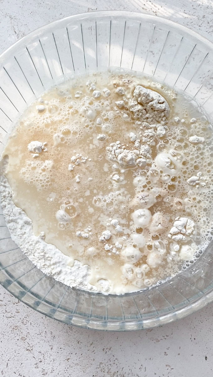 Lukewarm water added to the large transparent bowl of flour and yeast.