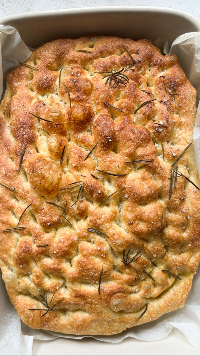 Focaccia baked and golden brown in its baking dish with rosemary and sea salt.