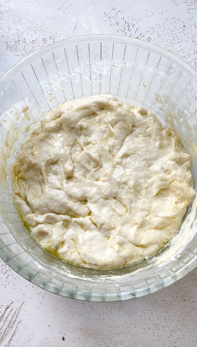 Focaccia dough before its first rise, in a large transparent bowl.