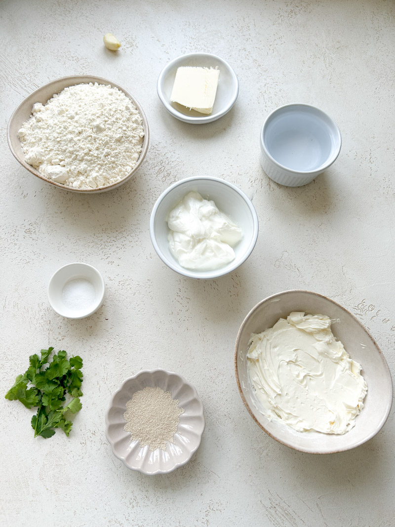 Les ingrédients pour préparer des cheese naans dans des assiettes et des bols blancs et beiges.