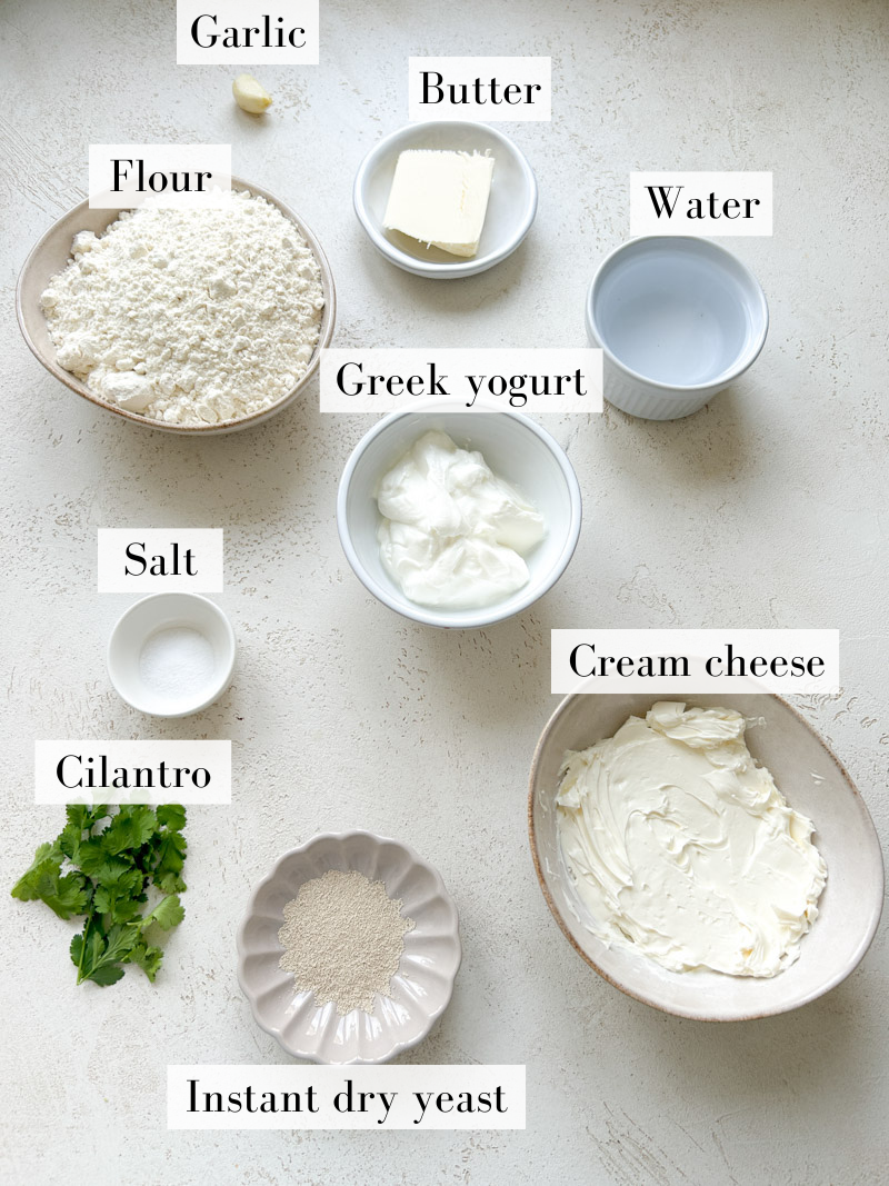 Ingredients to make garlic cheese naan in white and beige bowls and plates.