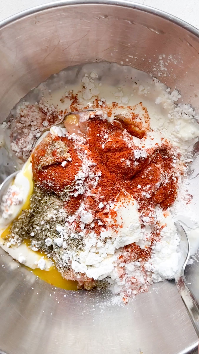 Œuf, fécule de maïs et crème sont ajoutés aux morceaux de poulet dans le bol en inox.