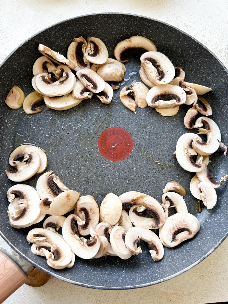 Sliced cremini mushrooms in a large grey pan.