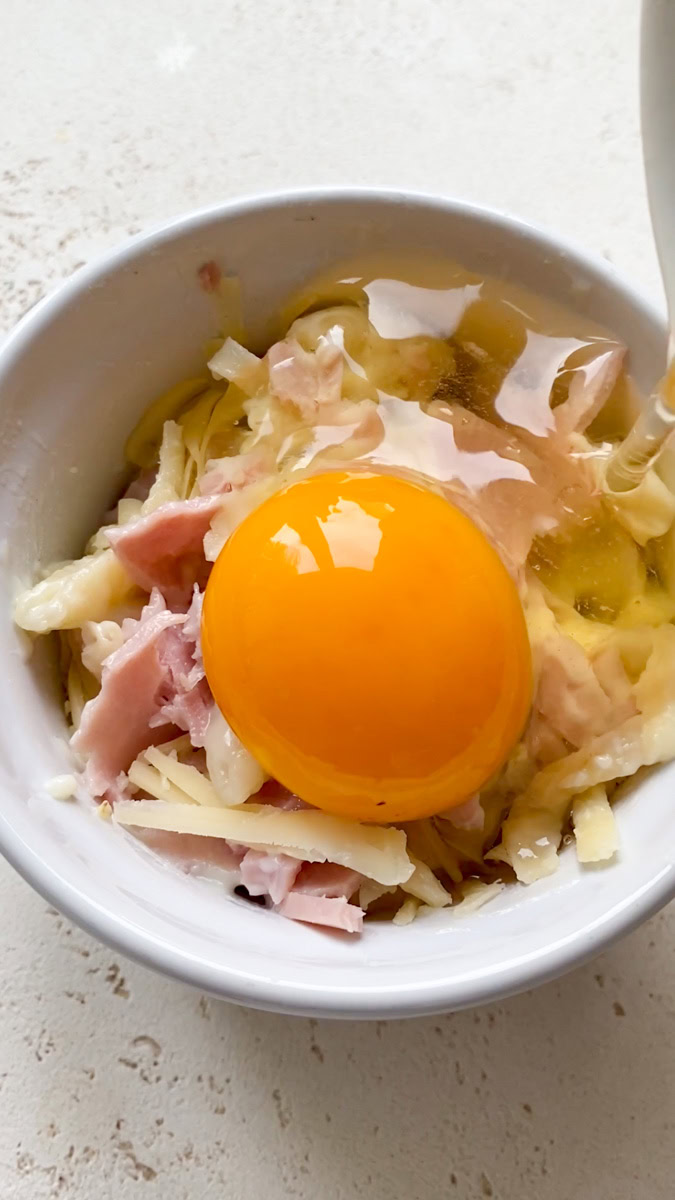 An egg is added to the mixture of pasta, béchamel, ham and cheese in the ramekin.