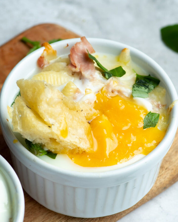 Egg cocotte in a white ramekin with a piece of focaccia that drips with egg yolk.