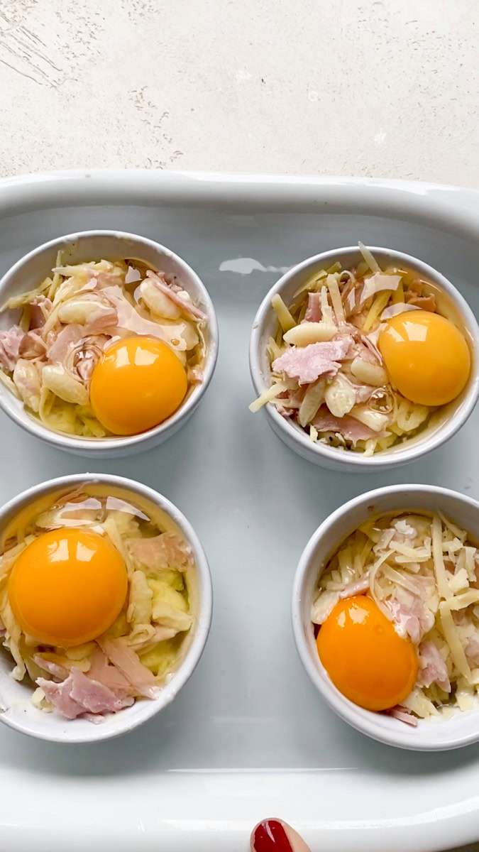 Four ramekins of eggs cocotte in a dish filled with water, ready to go into the oven to bake.