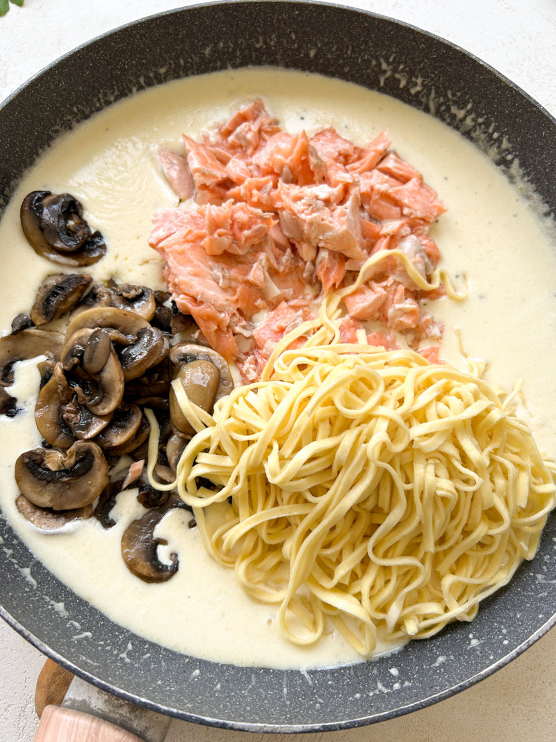 Sliced cremini mushrooms, crumbled salmon and cooked pasta in the large grey pan.