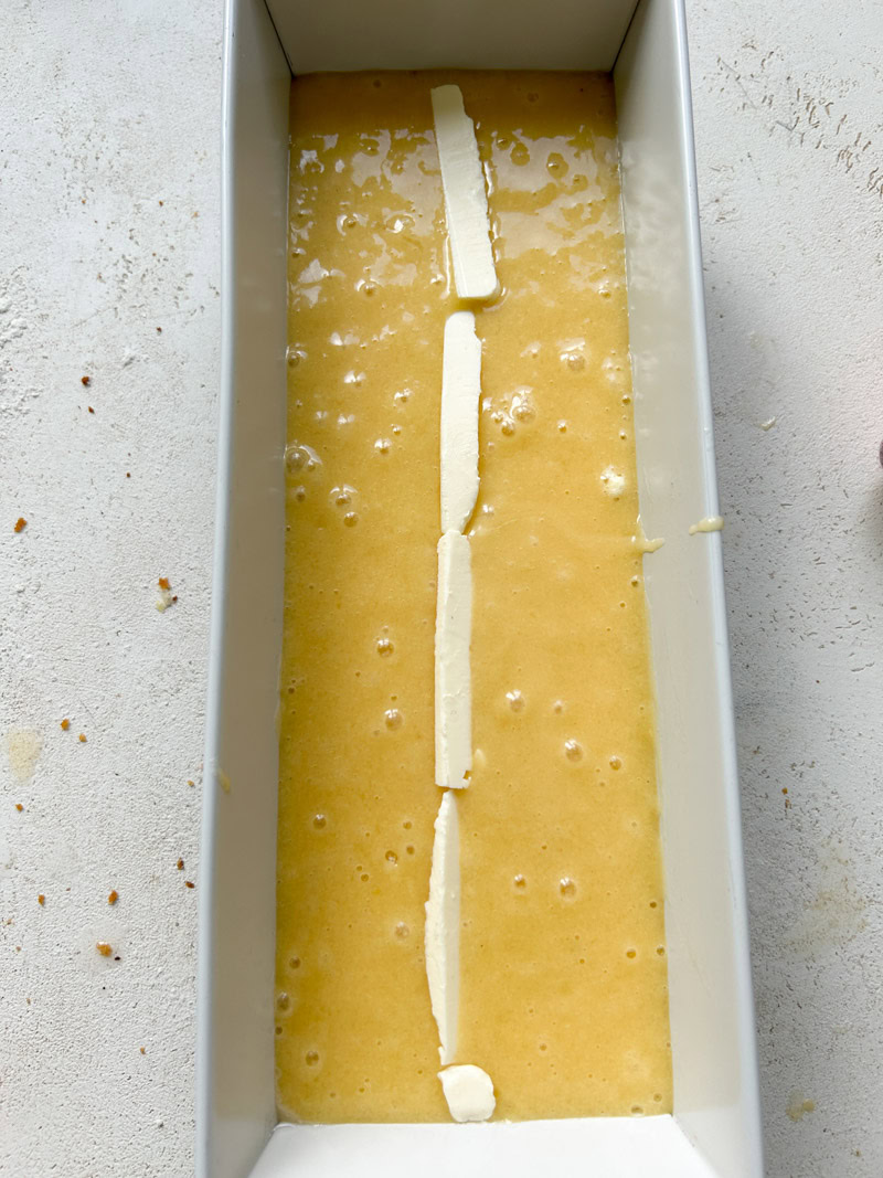 The pound cake batter is in a rectangular mold, with a few thin strips of butter in the middle.