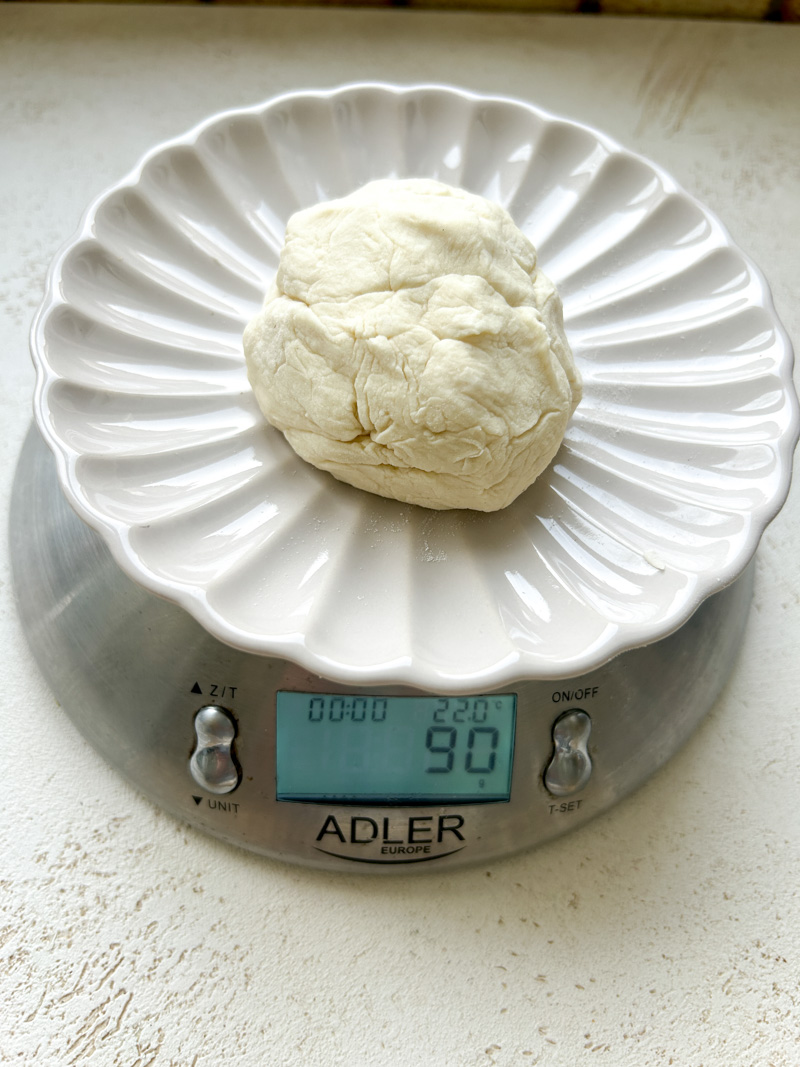 Assiette beige avec un pâton de pâte, sur une balance digitale de cuisine qui affiche 90 g.