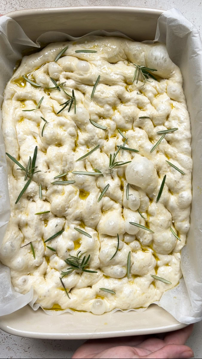 Dough in the baking dish, with large air bubbles, sea salt and rosemary.
