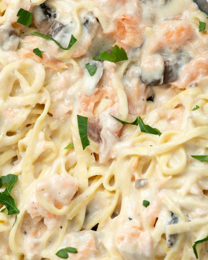 Salmon Alfredo pasta in a large skillet with fresh parsley and cremini mushrooms.