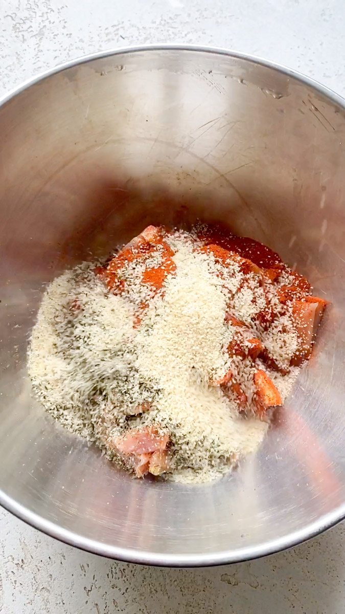 Ail en poudre, paprika et herbes de Provence sont ajoutés aux morceaux de poulet, dans le bol en inox.