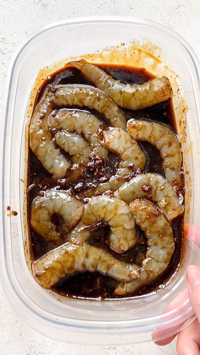 Teriyaki sauce and raw shrimp in a transparent container.