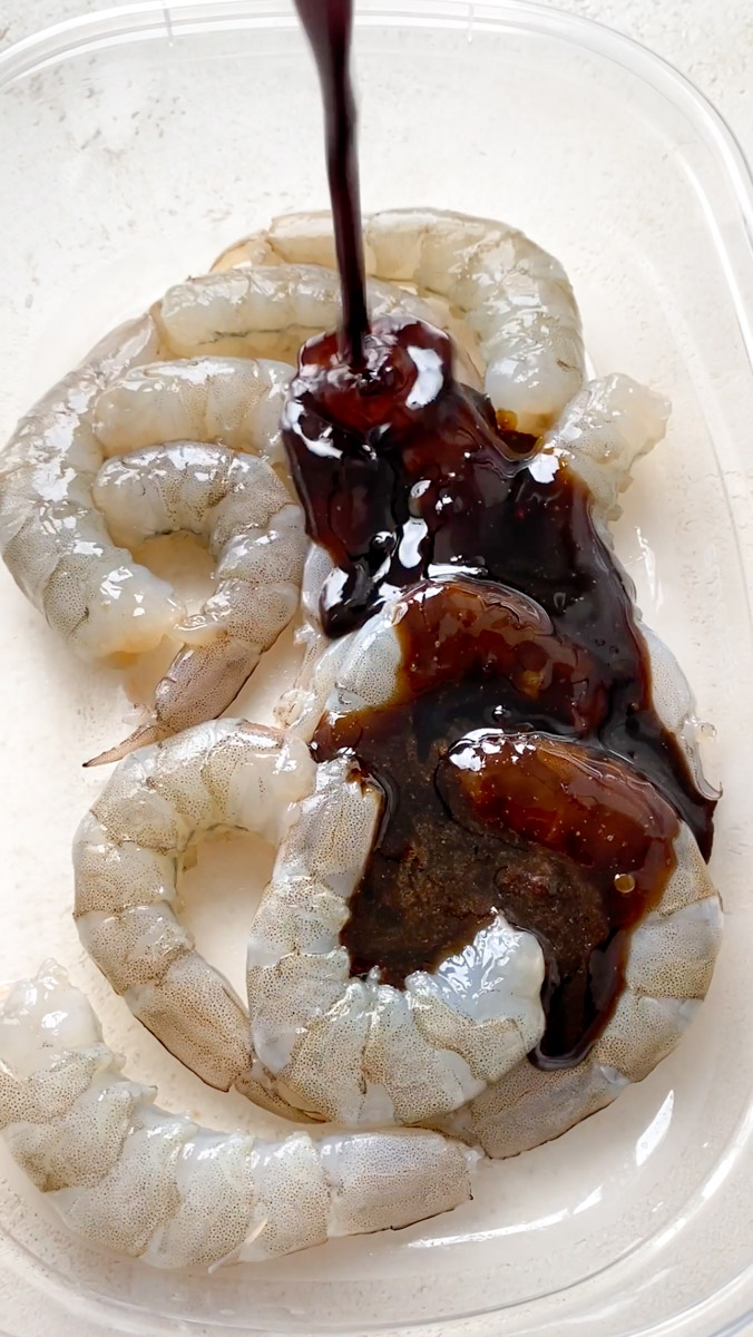 La sauce Teriyaki est versée sur les crevettes crues dans un récipient transparent.