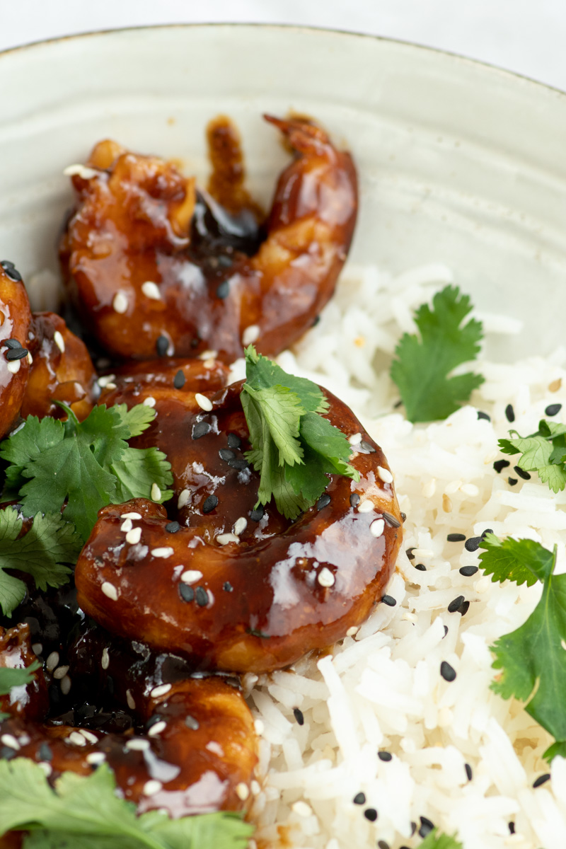 Teriyaki shrimp in a beige bowl with rice, sesame seeds and fresh cilantro.