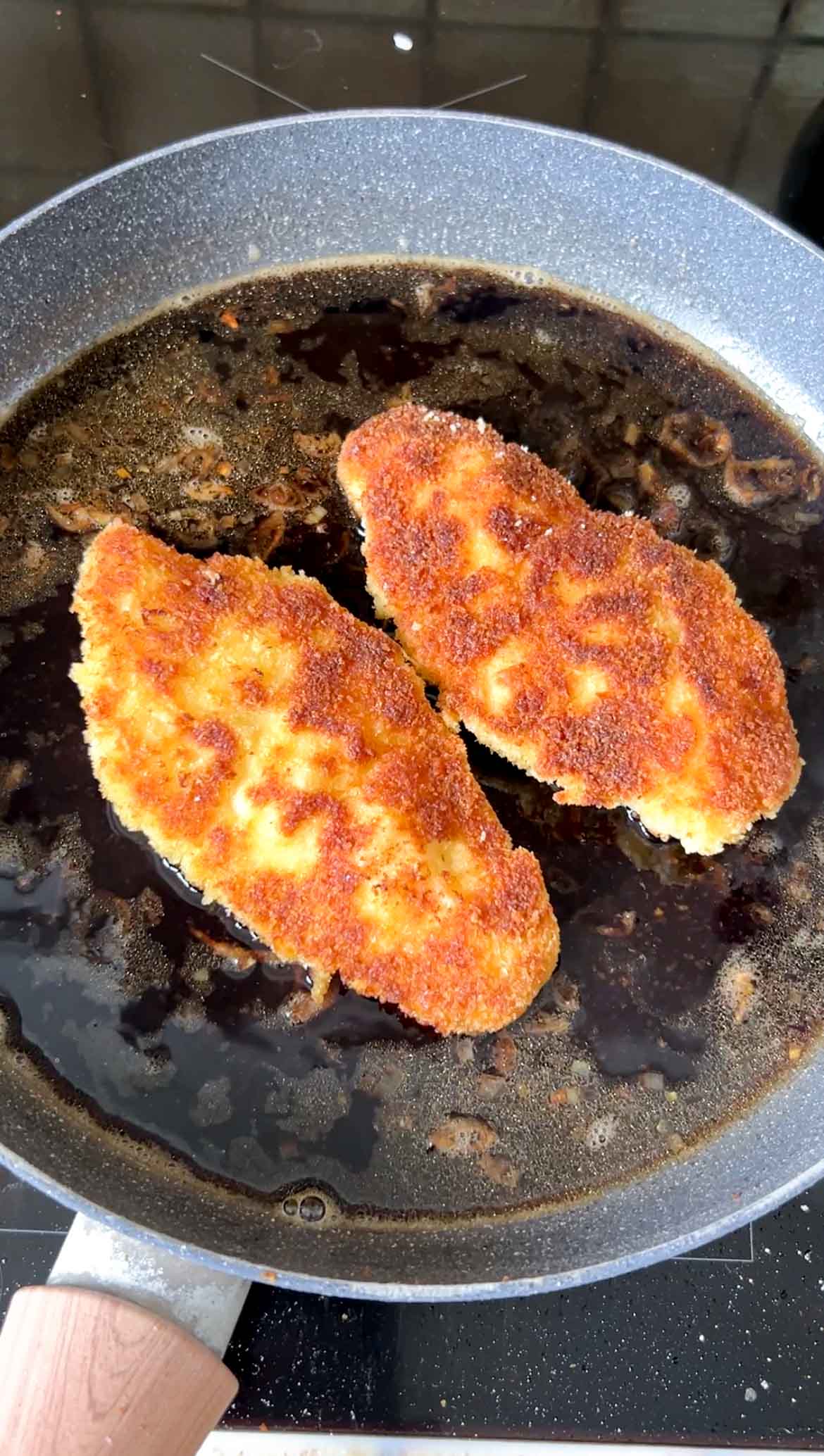 Breaded chicken cutlets back in the frying pan of sauce.