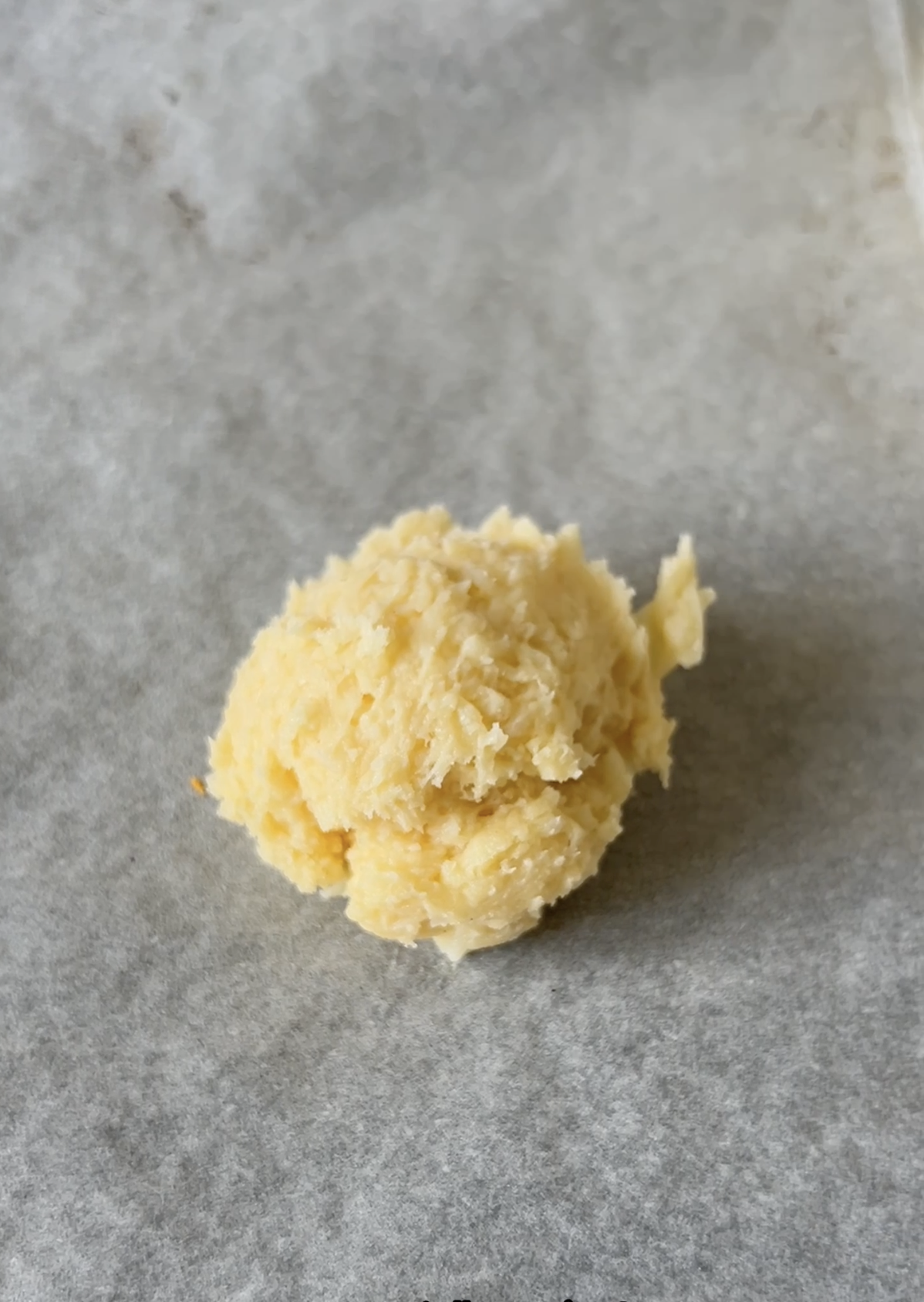 Boule de pâte à cookie salée déposée sur une feuille de papier cuisson, avant la cuisson.