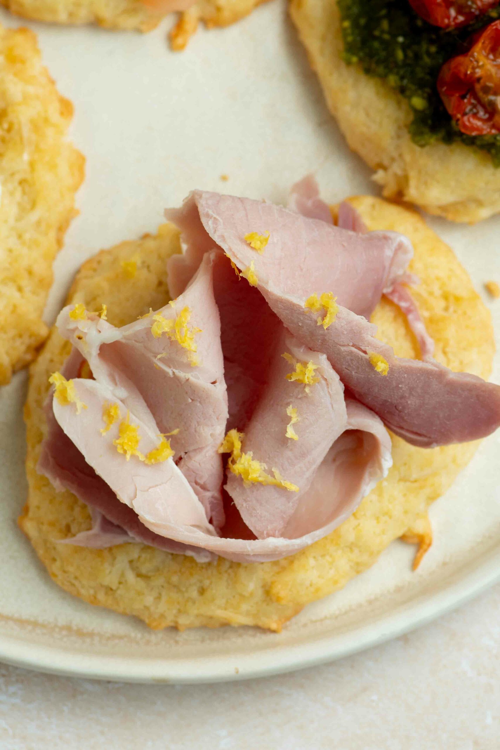 A cookie placed on a plate and garnished with a slice of ham and lemon zest.