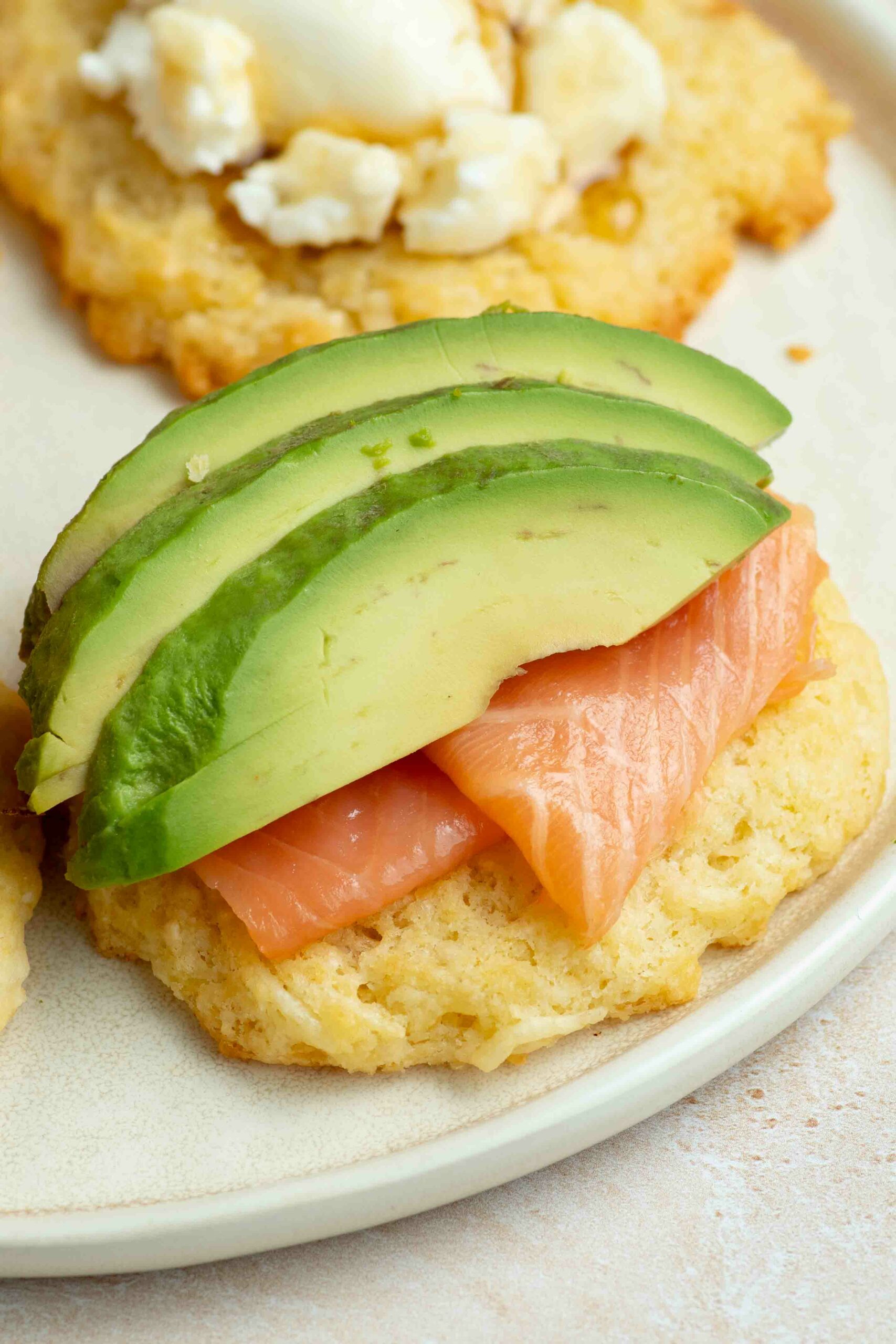 A cookie placed on a plate and garnished with smoked salmon and three slices of avocado.