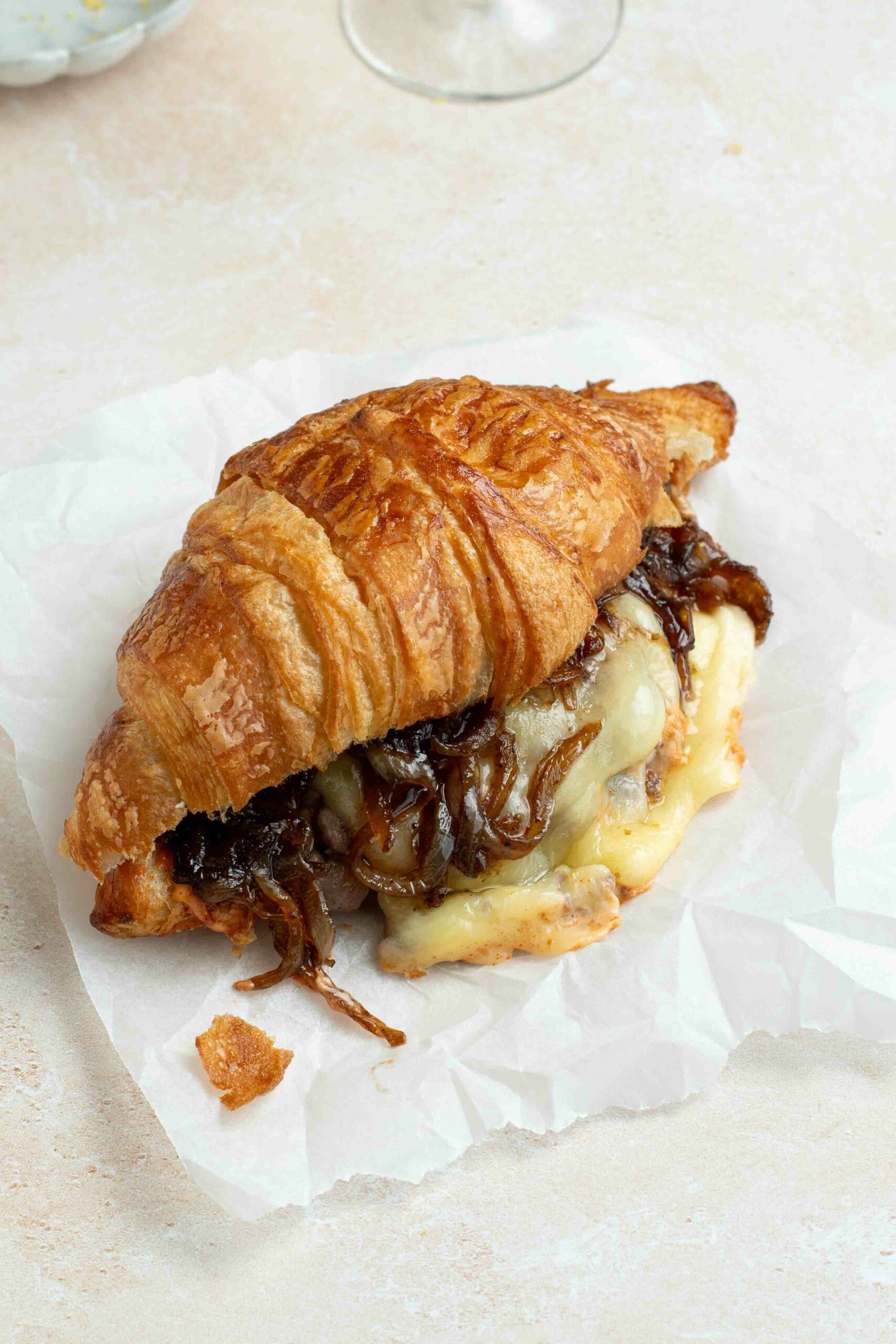Croissant burger on a sheet of baking paper, with onion confit and runny cheese.