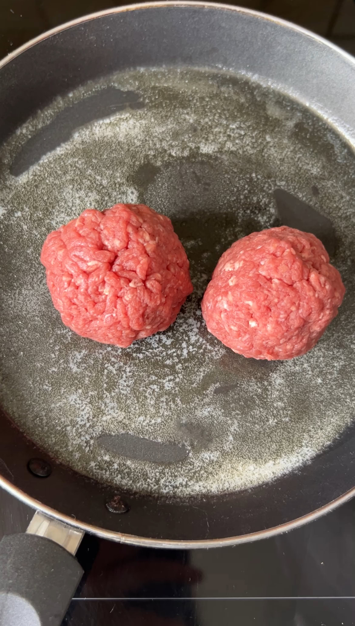Two meatballs in a dark frying pan with butter.