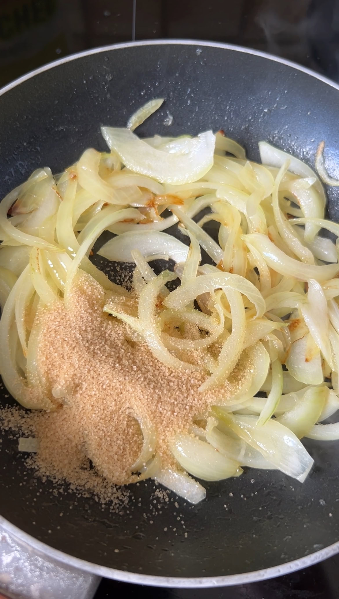 Cassonade ajoutée à la poêle de lamelles d'oignon qui cuisent.