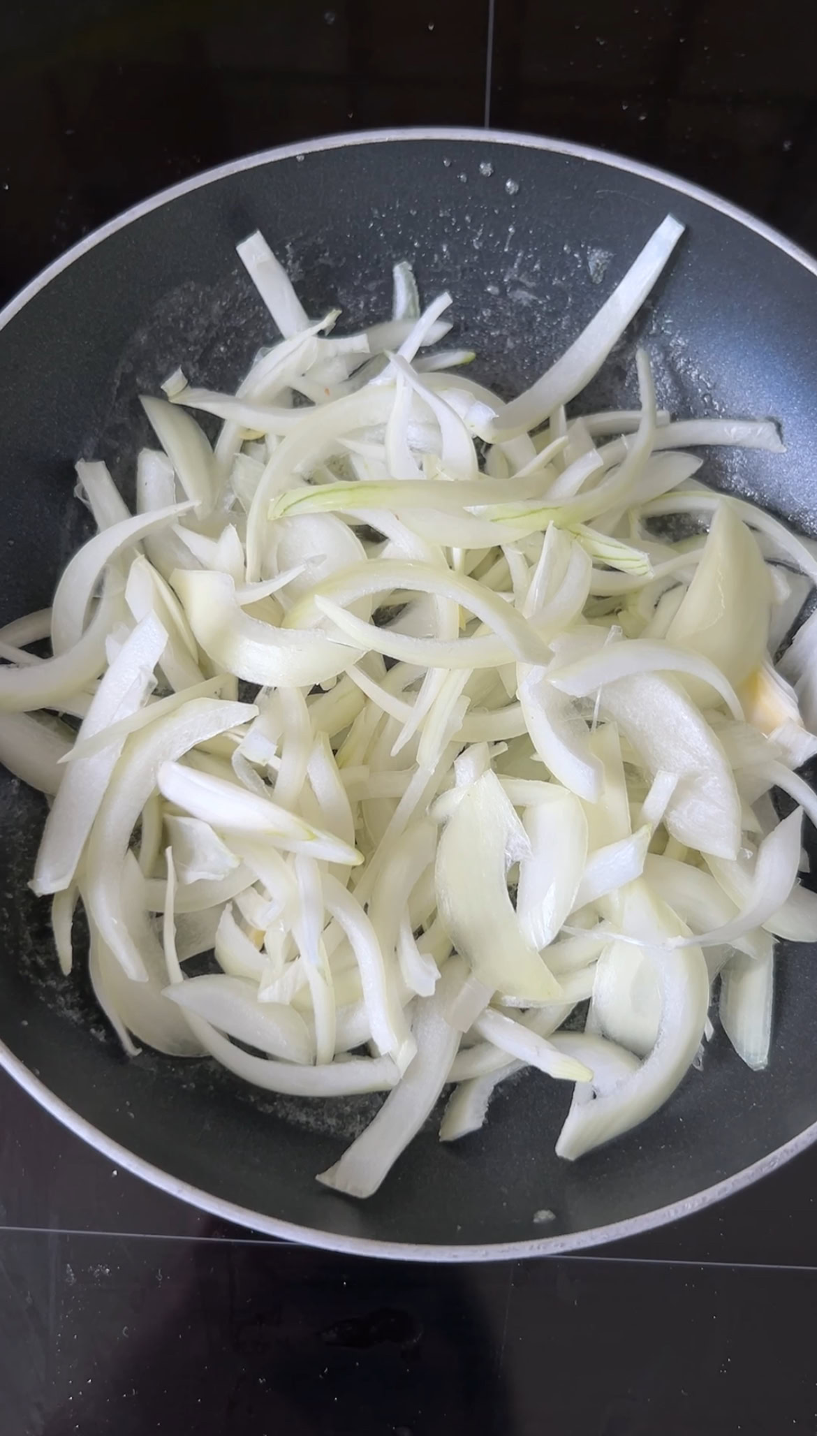 Onion strips cooking in a black frying pan with butter.