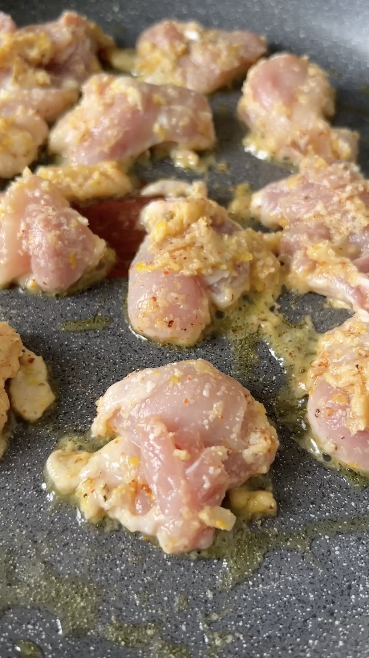 Chicken pieces, with lemon zest and Parmesan cheese, cooking in the pan.