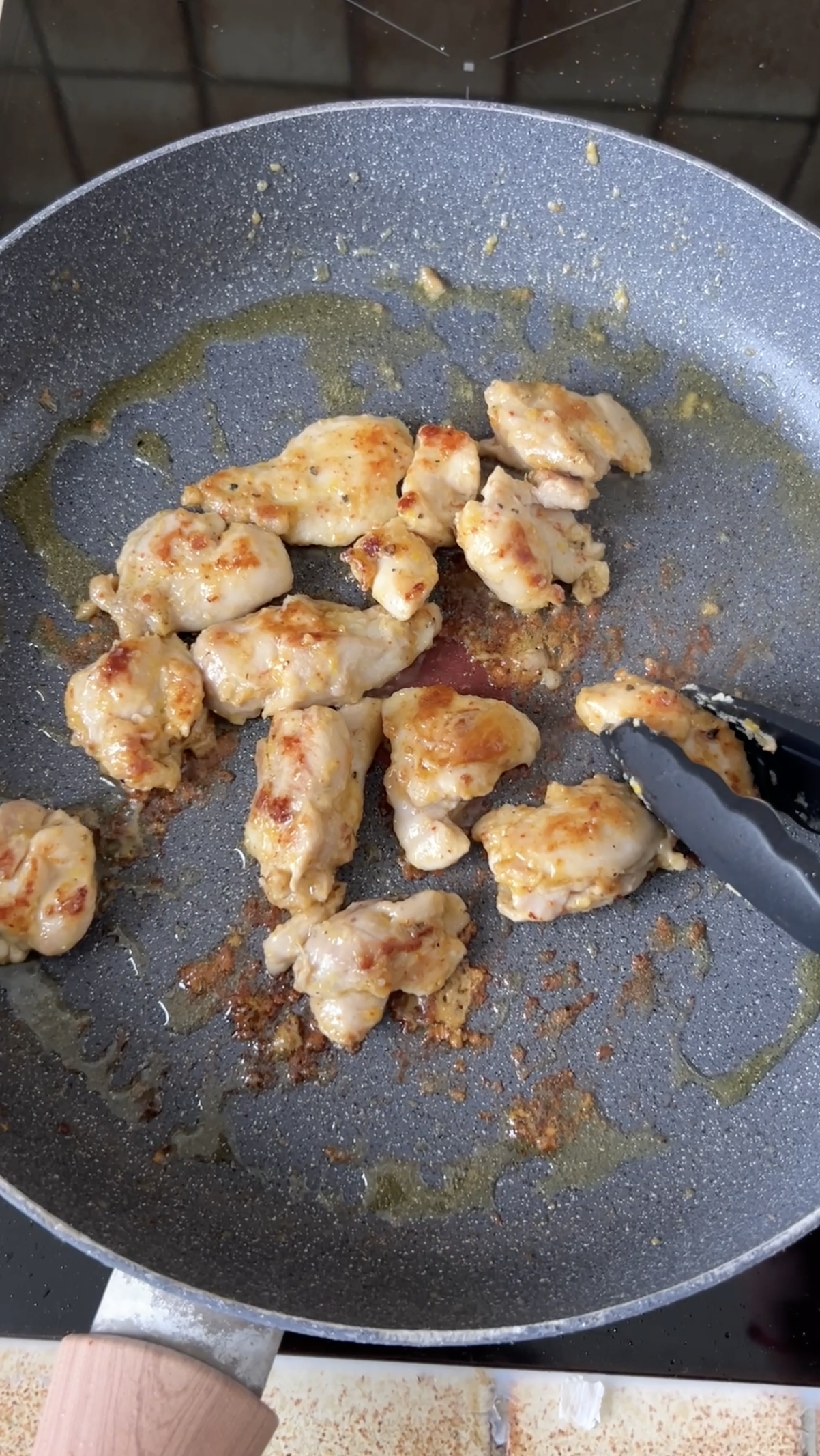 Golden chicken pieces, removed from the pan with black tongs.