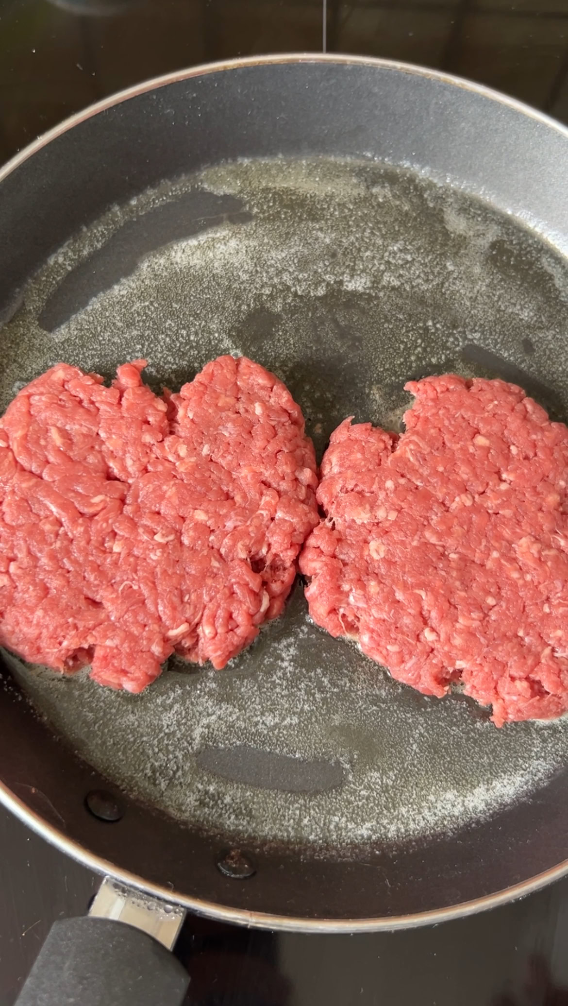 Two pieces of minced meat cooking in the black pan with melted butter.