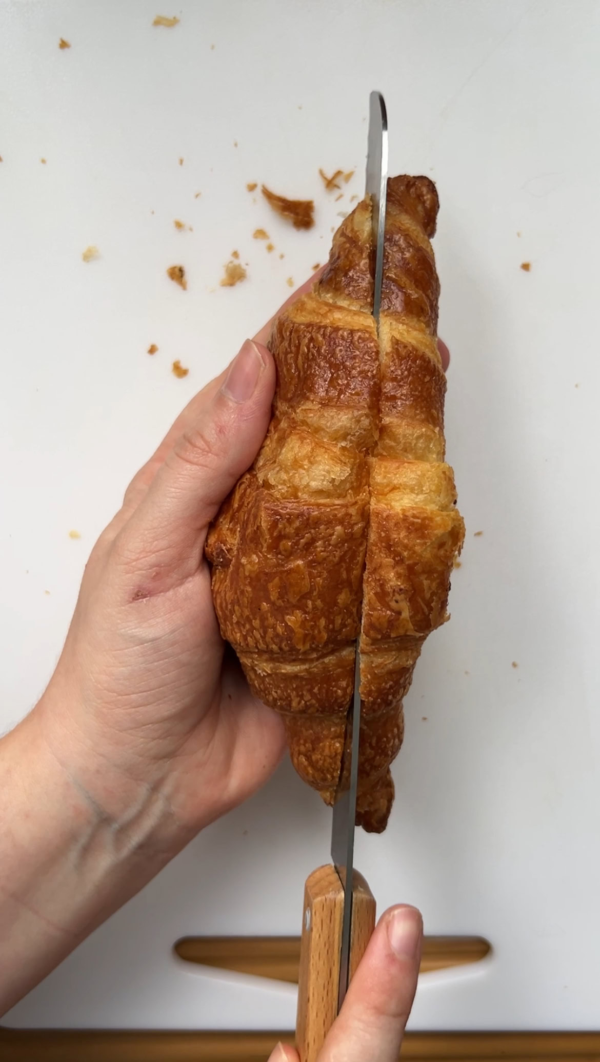 Croissant held in one hand and cut lengthwise by a bread knife.